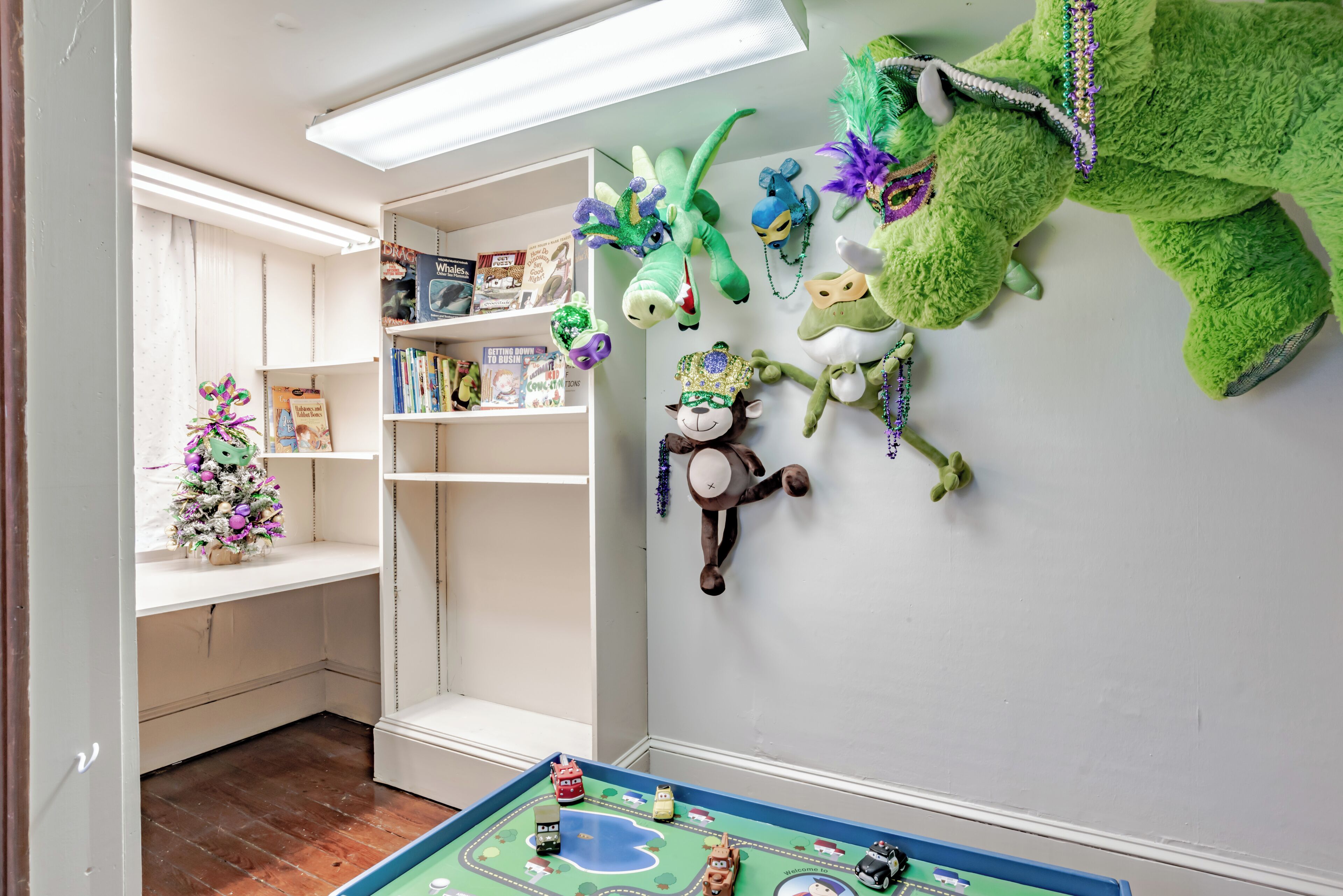 A room with a play area, including a toy car and a board game. Shelves with books and toys are visible.