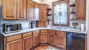 A kitchen with wooden cabinets, a microwave, a dishwasher, and a window with stained glass. - Central Location Historic Grandeur (Mobile)