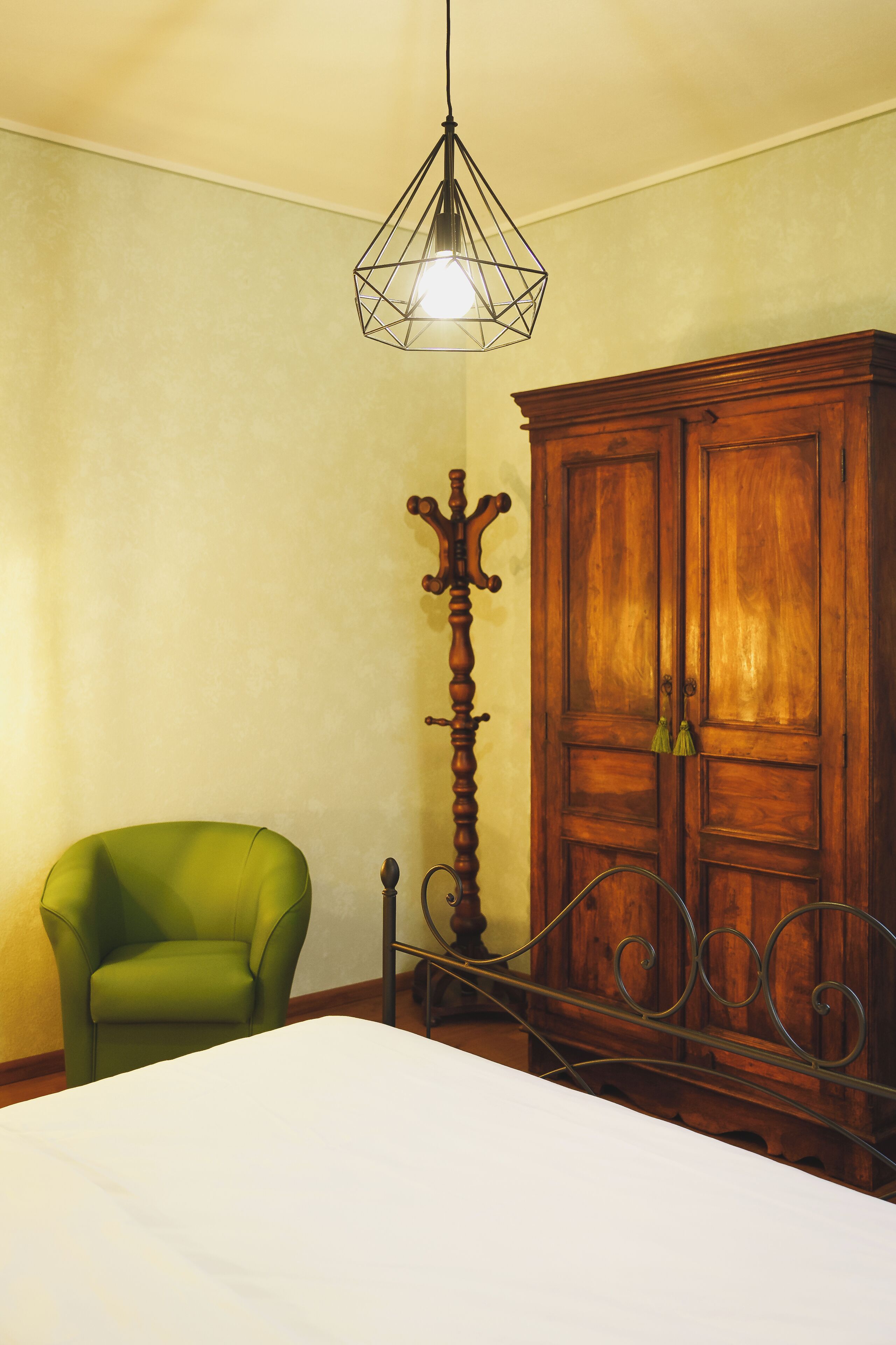 A room with a bed, a green armchair, a wooden wardrobe, and a tall floor lamp.