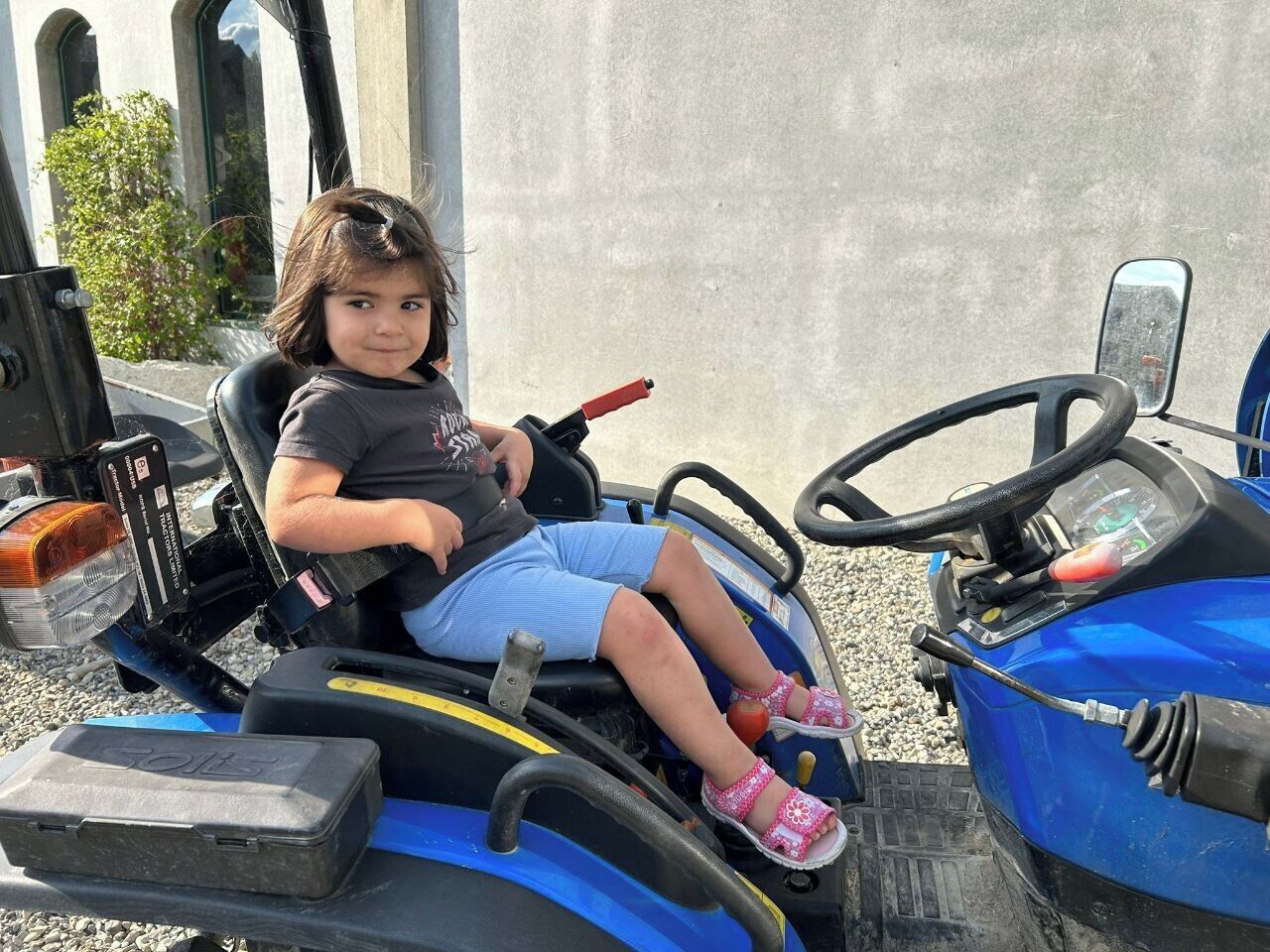 A child seated on a blue tractor-like vehicle with a steering wheel and a control panel.