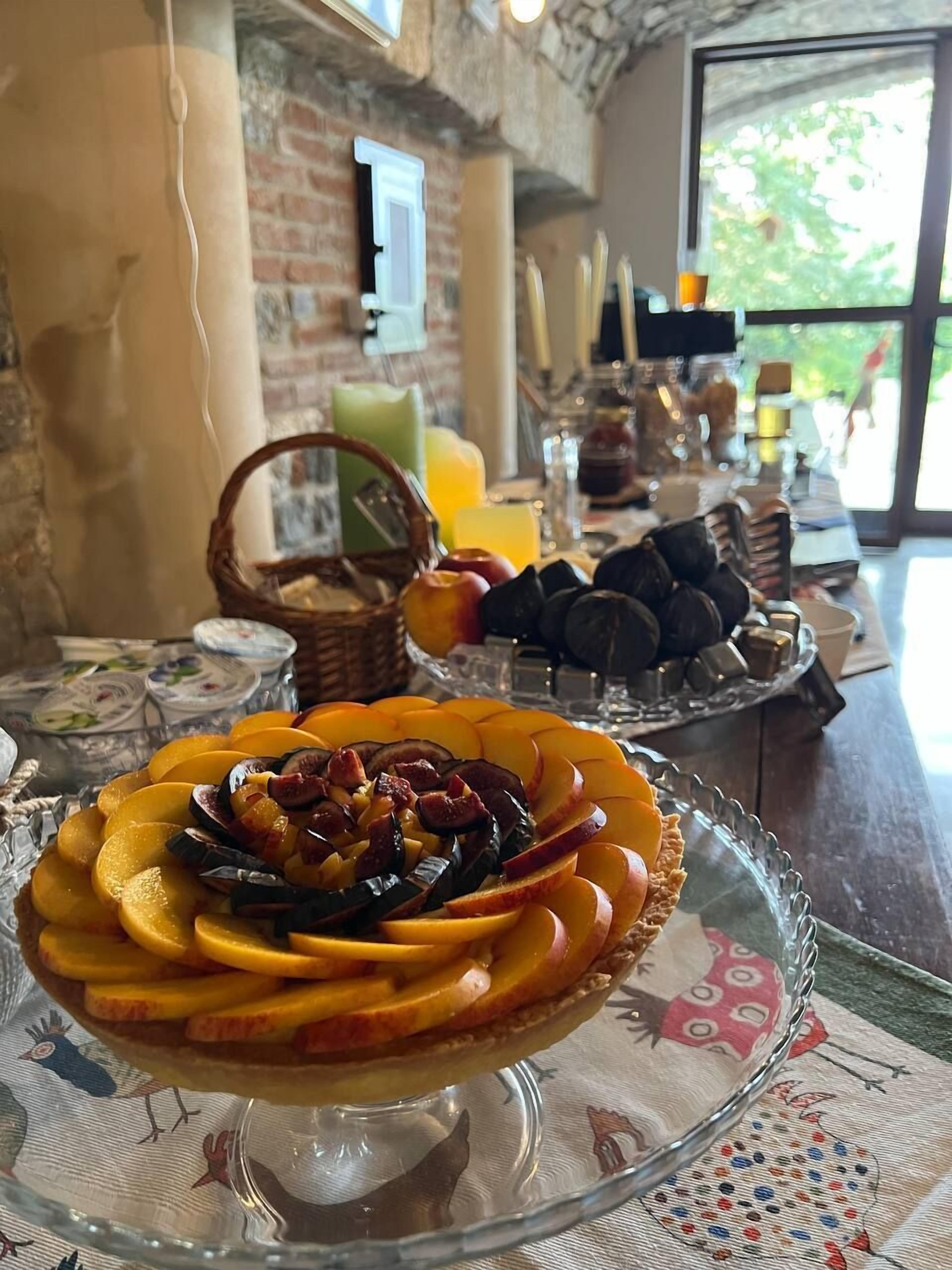 A breakfast setting with a fruit tart on a glass stand, a basket of bread, and a selection of pastries on a table.