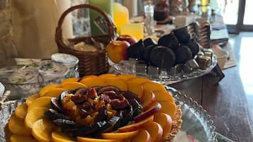 A breakfast setting with a fruit tart on a glass stand, a basket of bread, and a selection of pastries on a table.