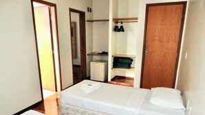Een slaapkamer met een bed, een houten garderobe, een klein bureau en een plank met opgevouwen kleding.
