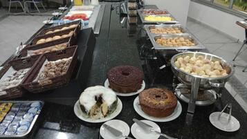 Buffet com diversos alimentos, incluindo bolos, doces e frutas.