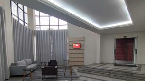 Een ruime lobby met een grijze bank, een klein tafeltje en een aan de muur bevestigde televisie.