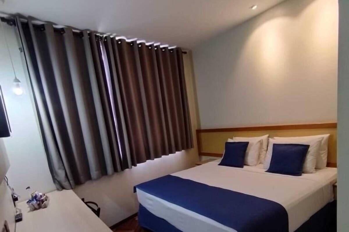 Una habitación de hotel con cama, escritorio y ventana con cortinas.