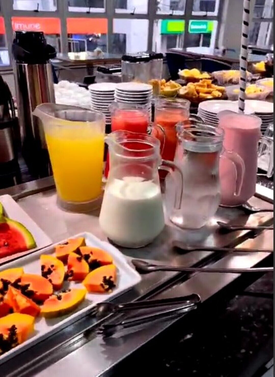 A breakfast buffet with various fruit options, beverages, and utensils.