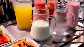 A breakfast buffet with various fruit options, beverages, and utensils.