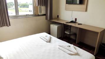 Une chambre d’hôtel avec un lit, un bureau, une chaise, une télévision et une fenêtre avec des rideaux.