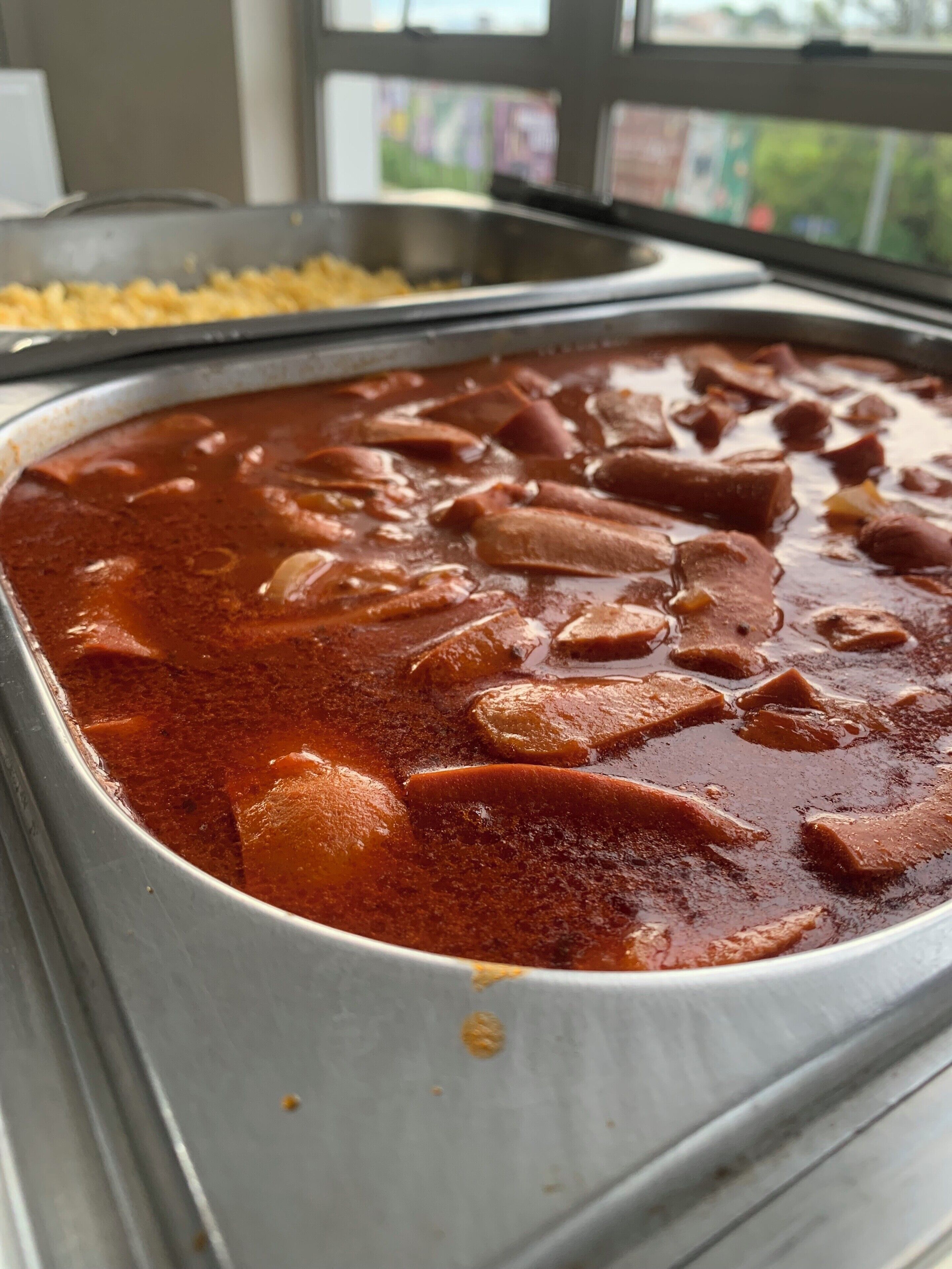 A buffet with a large container of red stew, possibly chili, with chunks of meat.