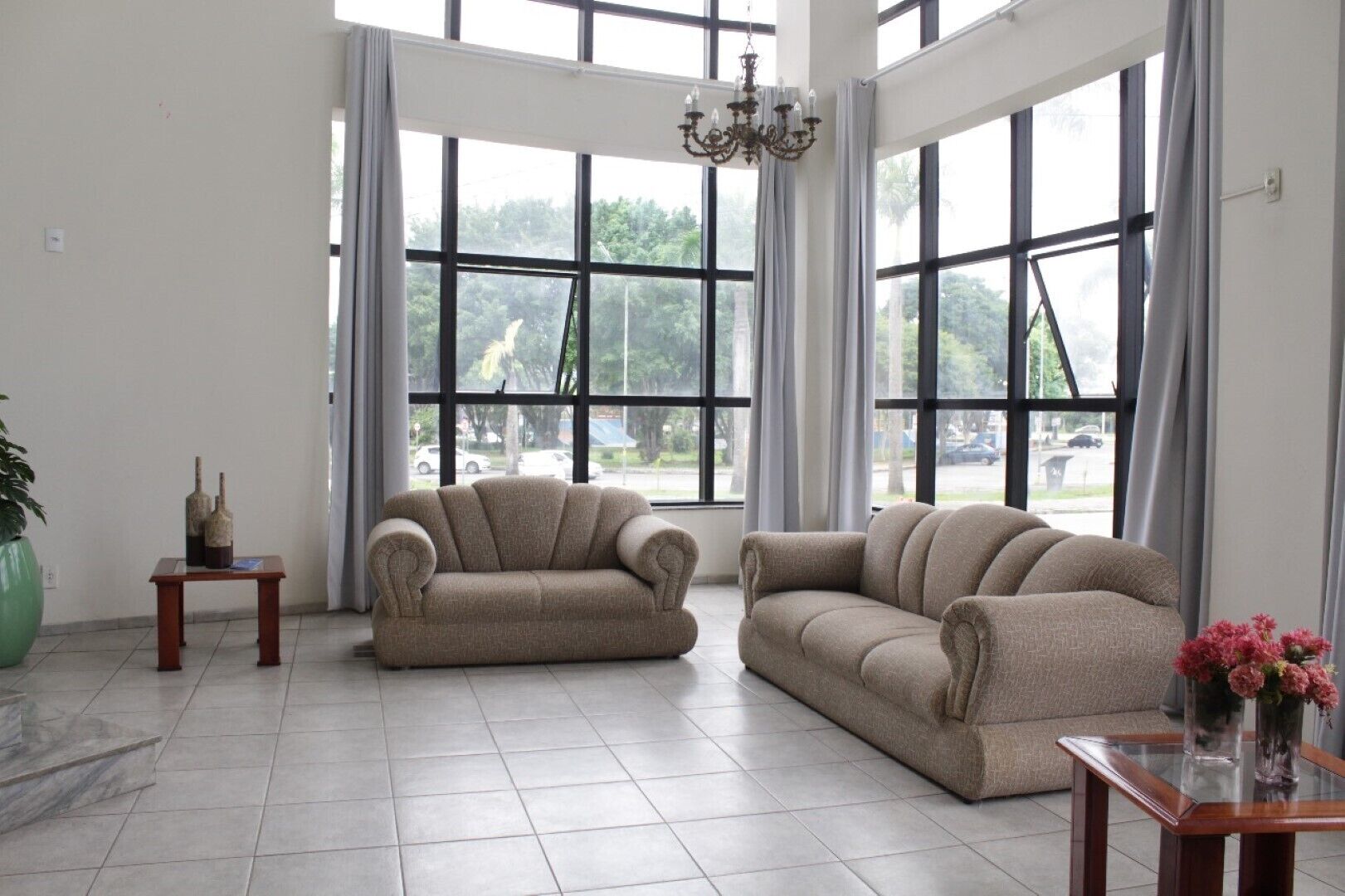 Amplia sala de estar con dos sofás color beige, una mesa de centro de madera, un candelabro y ventanas grandes que ofrecen vistas al exterior.