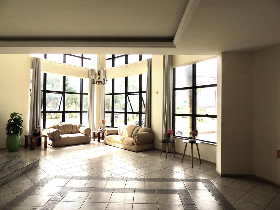 A spacious living room with large windows, a chandelier, and a green plant.