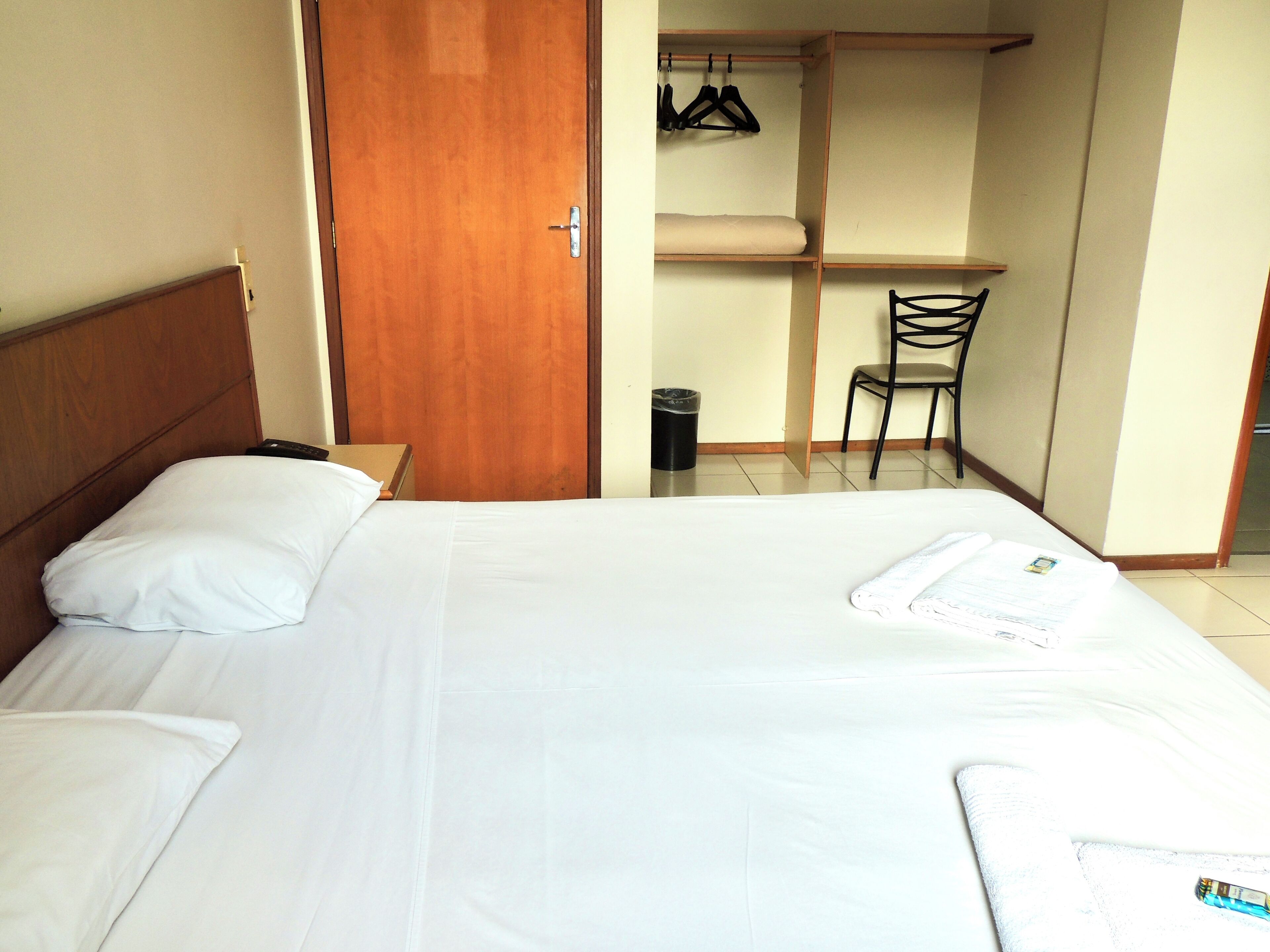 A hotel room with a bed, a wooden headboard, a chair, and a desk with a chair.