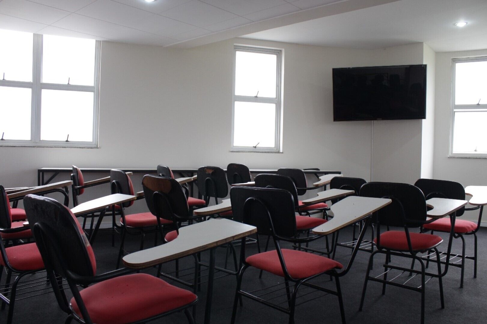 A classroom with desks and chairs, large windows, and a mounted television.