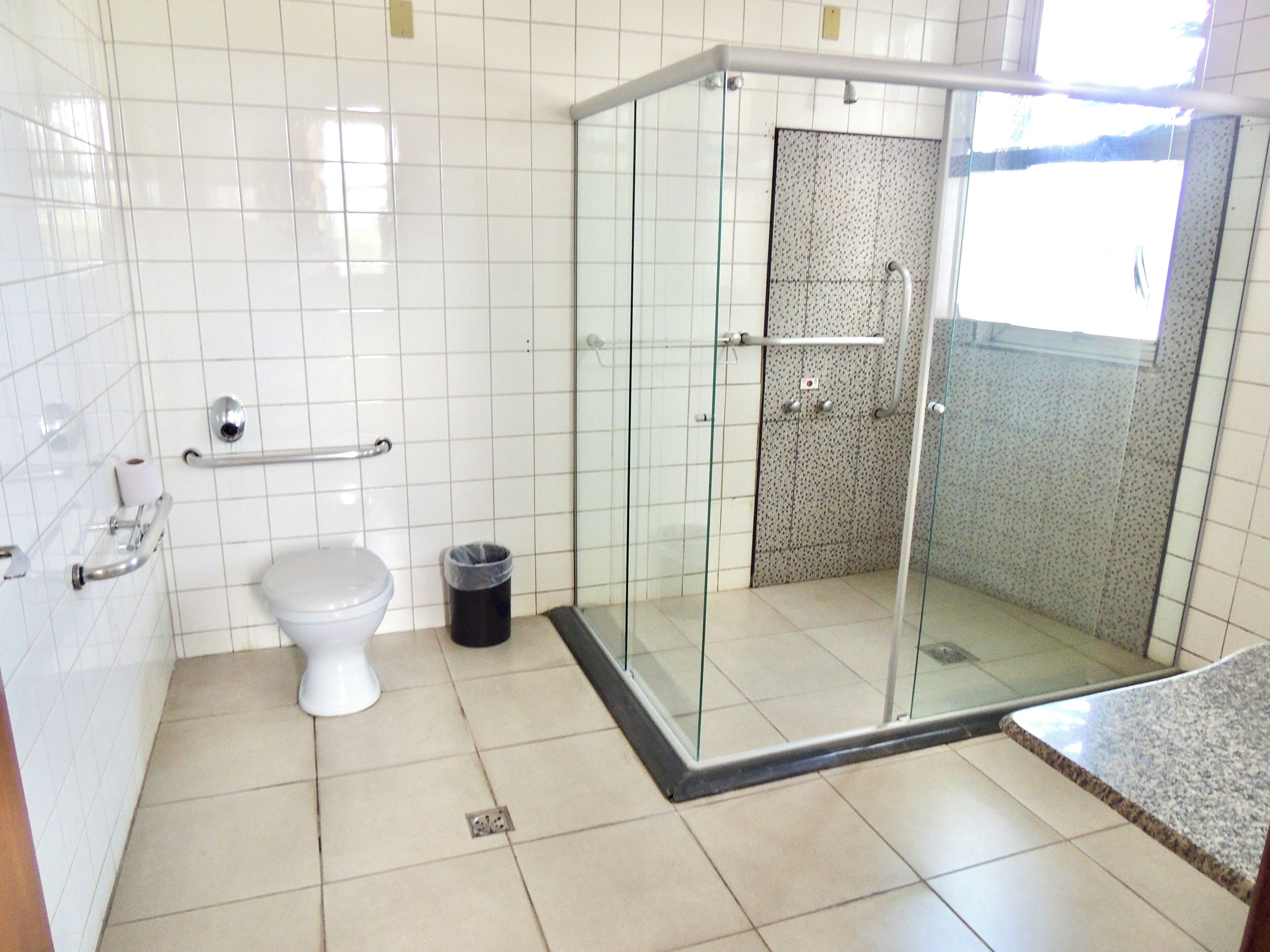 Een badkamer met toilet, een prullenbak, een glazen douchecabine en betegelde wanden.