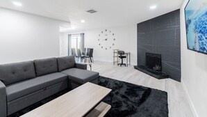A modern living room with a sectional sofa, a coffee table, a fireplace, and a wall clock.