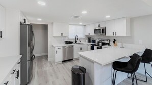 A modern kitchen with white cabinetry, stainless steel appliances, and a central island with bar stools.