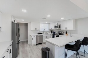 Una cocina moderna con armarios blancos, electrodomésticos de acero inoxidable y una isla central con taburetes de bar.