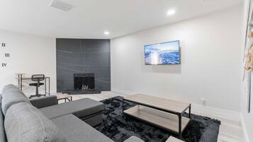 Una sala de estar moderna con un sofá seccional, un televisor de pantalla plana montado en la pared y una chimenea con un revestimiento texturizado en la pared de fondo.