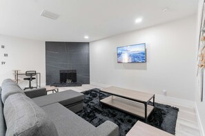 Una sala de estar moderna con un sofá seccional, un televisor de pantalla plana montado en la pared y una chimenea con un revestimiento texturizado en la pared de fondo.