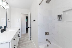 A modern bathroom with a white marble wall, a bathtub, and a shower area. - 5Mins to Fremont! 10Mins to Strip! Sleeps 8! (Las Vegas)