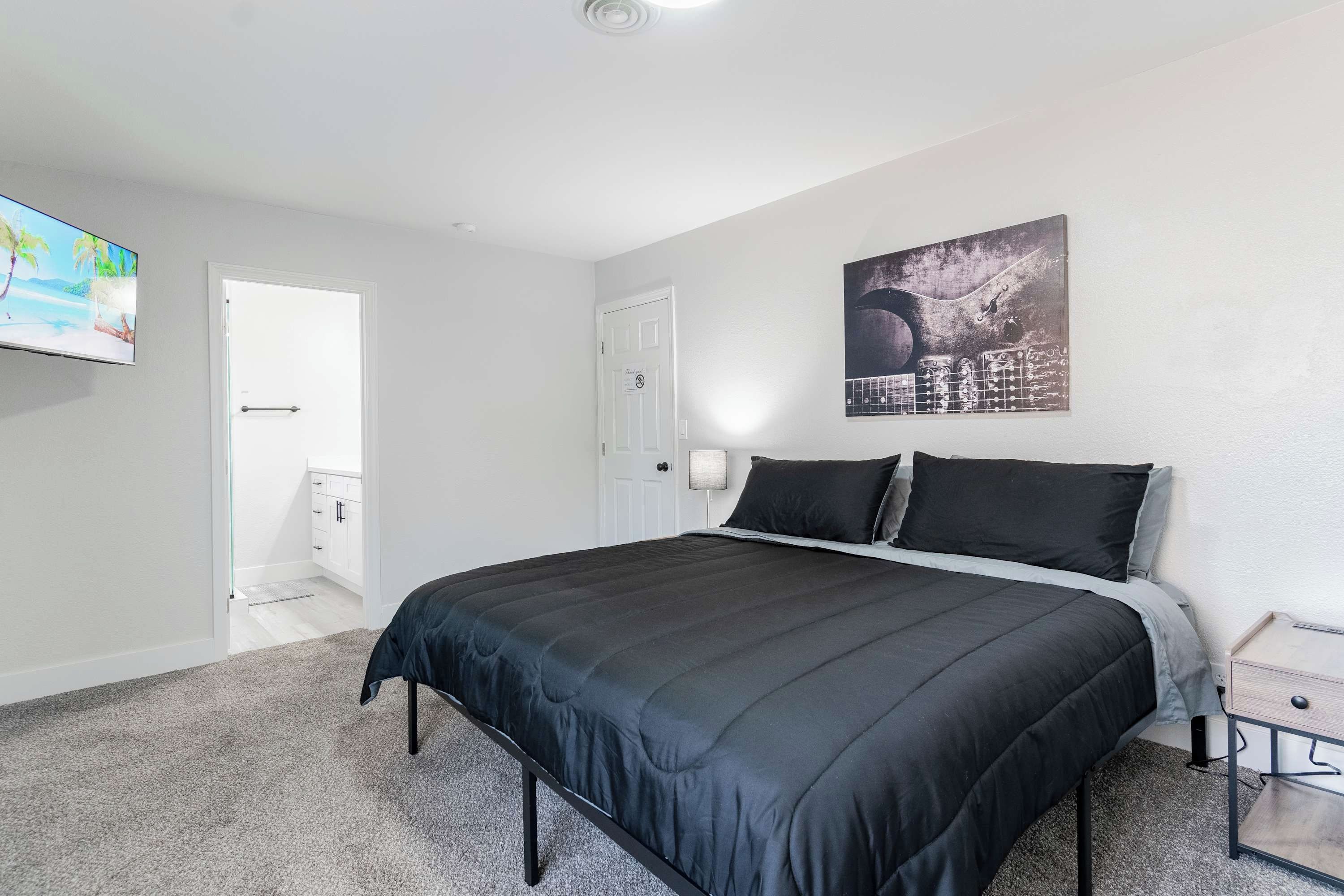 Ein Schlafzimmer mit einem Bett, einem Fernseher, einer Tür und einem an der Wand hängenden Kunstwerk.