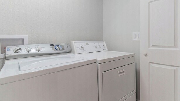 A laundry area with a front-loading washer and dryer, a white wall, and a door.