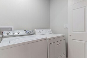 A laundry area with a front-loading washer and dryer, a white wall, and a door.