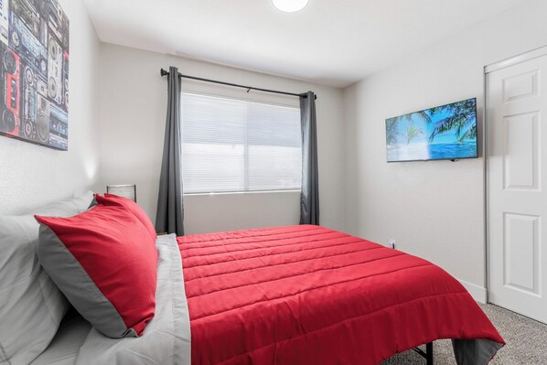 Un dormitorio con cama, ventana con cortinas, un cuadro en la pared y una puerta.