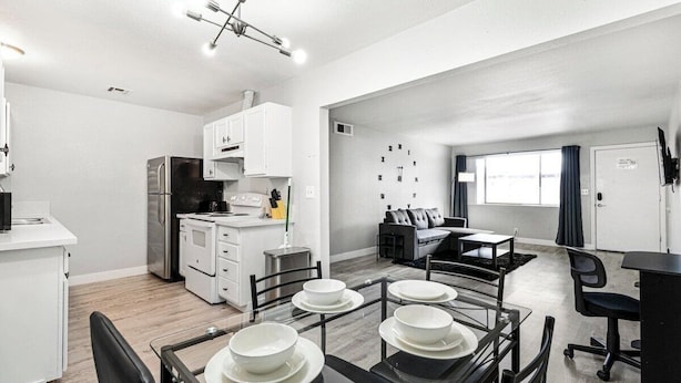 A modern kitchen with white cabinetry, a stainless steel refrigerator, and a dining area with a glass table and chairs. - Cozy 1 Bed, Sleeps 4! Near Strip! Perfect GetAway! (Las Vegas)