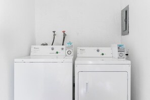 Two white Whirlpool washing machines with control panels, hoses, and a water meter on a white wall.