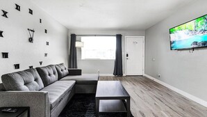 A modern living room with a sectional sofa, a coffee table, a flat-screen TV, and a large window with curtains. - Cozy 1 Bed, Sleeps 4! Near Strip! Perfect GetAway! (Las Vegas)