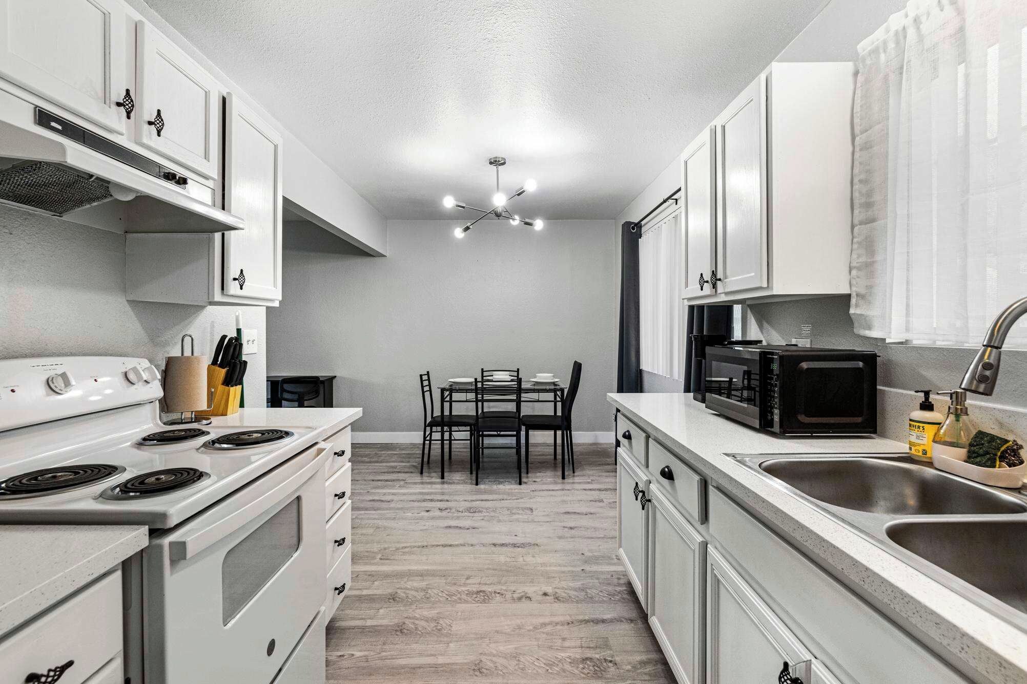 A modern kitchen with white cabinetry, a dining table with chairs, a microwave, and a sink.