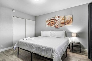 A modern bedroom with a large bed, a bedside table with a lamp, and a wall-mounted abstract painting.