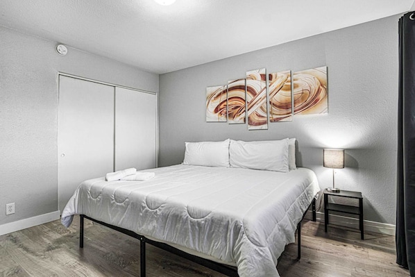 A modern bedroom with a large bed, a bedside table with a lamp, and a wall-mounted abstract painting.