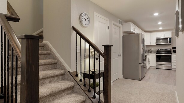 A modern kitchen with stainless steel appliances, a wooden staircase, and a clock on the wall. - 1 Bedroom/ 1 Bath Suite in The Copperleaf Villas (Centennial)