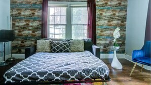 A bedroom with a bed, a blue chair, a white vase with an orchid, and a window with curtains. - Cozy King bed and Queen Sofa bed Apt (Decatur)