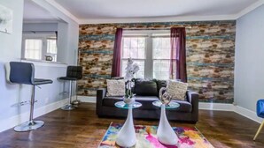 A living room with a dark wood floor, a black sofa, two white vases, and a colorful rug. - Cozy King bed and Queen Sofa bed Apt (Decatur)