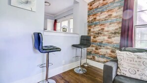A modern living room with two bar stools, a sofa with patterned cushions, and a wooden accent wall. - Cozy King bed and Queen Sofa bed Apt (Decatur)