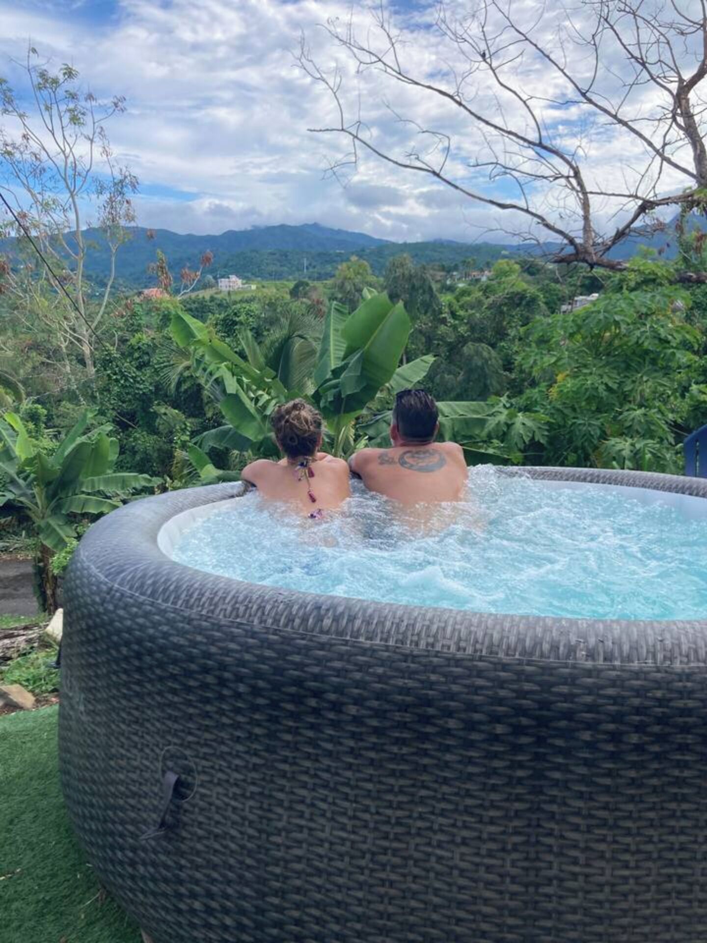 Two people relaxing in a hot tub with a view of a lush landscape and mountains in the background.