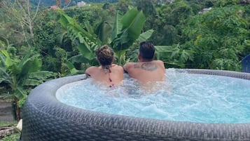 Two people relaxing in a hot tub with a view of a lush landscape and mountains in the background.