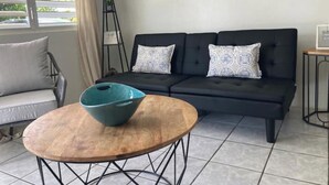 A modern living room with a black sofa, patterned cushions, a wooden coffee table, and a floor lamp. - #G Tropical Rainforest Retreat Ocean View w/hottub (Luquillo)