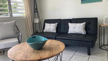 A modern living room with a black sofa, patterned cushions, a wooden coffee table, and a floor lamp.