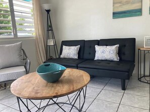 Een moderne woonkamer met een zwarte bank, gekleurde kussens, een houten salontafel en een vloerlamp.