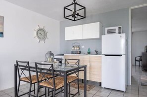 Une cuisine compacte avec des meubles blancs, un réfrigérateur blanc et une table à manger avec quatre chaises.