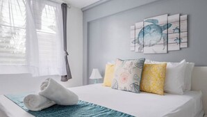 A neatly made bed with a blue patterned bedspread, a pair of rolled towels, and multiple pillows in yellow and white. - #G Tropical Rainforest Retreat Ocean View w/hottub (Luquillo)