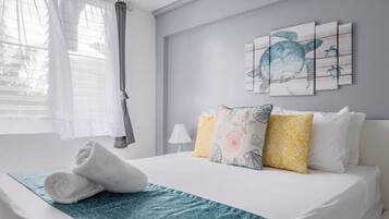 A neatly made bed with a blue patterned bedspread, a pair of rolled towels, and multiple pillows in yellow and white.
