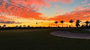 Ein Golfplatz bei Sonnenuntergang mit blauem Himmel und Palmen.