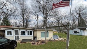 A residential property with a detached garage, a covered outdoor seating area, and a flagpole with an American flag. - Lakeside Haven  (Houghton Lake)
