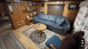 A cozy room with a wooden interior, a grey sofa, a small round table, and a blue chair. - Lakeside Haven  (Houghton Lake)